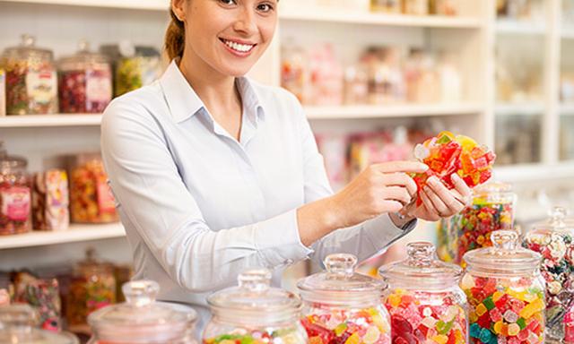 Shop assistant arranging jars of colourful sweets behind a bright Stranraer confectionery counter