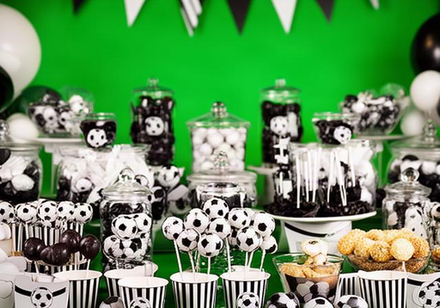 Football-themed sweet table with black and white sweets, striped paper cups and a green party backdrop