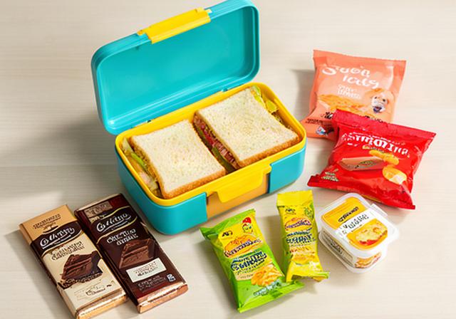 Chocolate bars and savoury snacks arranged beside a child's colourful lunchbox