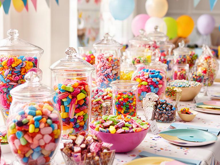 Colourful sweet table with glass jars, pick-and-mix sweets and party decorations in a bright event room