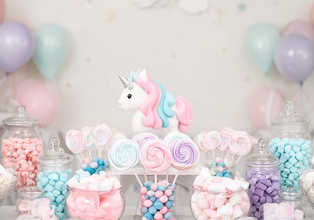 Pastel unicorn-themed sweet table with jars of pink and blue confectionery at a children's birthday party